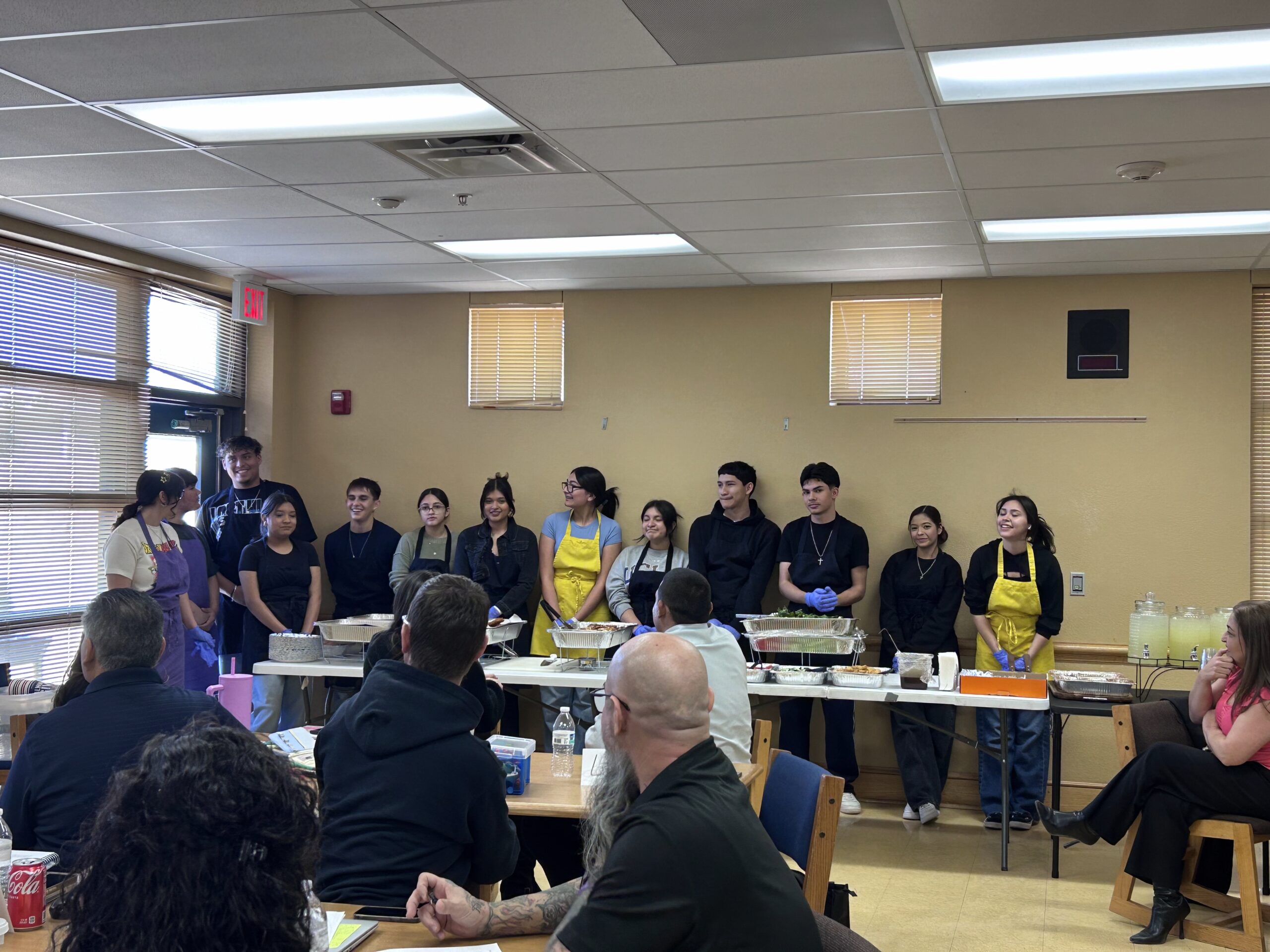 Teenagers in aprons presenting food to group